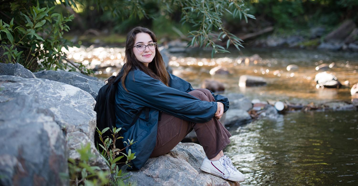 Julie Gentile sits beside a creek in the middle of the woods.