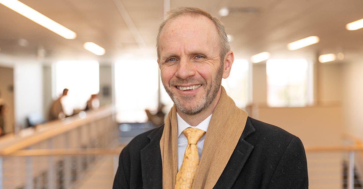 Kai Larsen in a jacket and scarf, standing in the open Rustandy Building atrium.