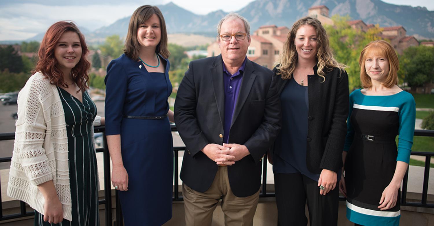 Four women surround Mark Meaney in a professional photo in front of the Flatirons.