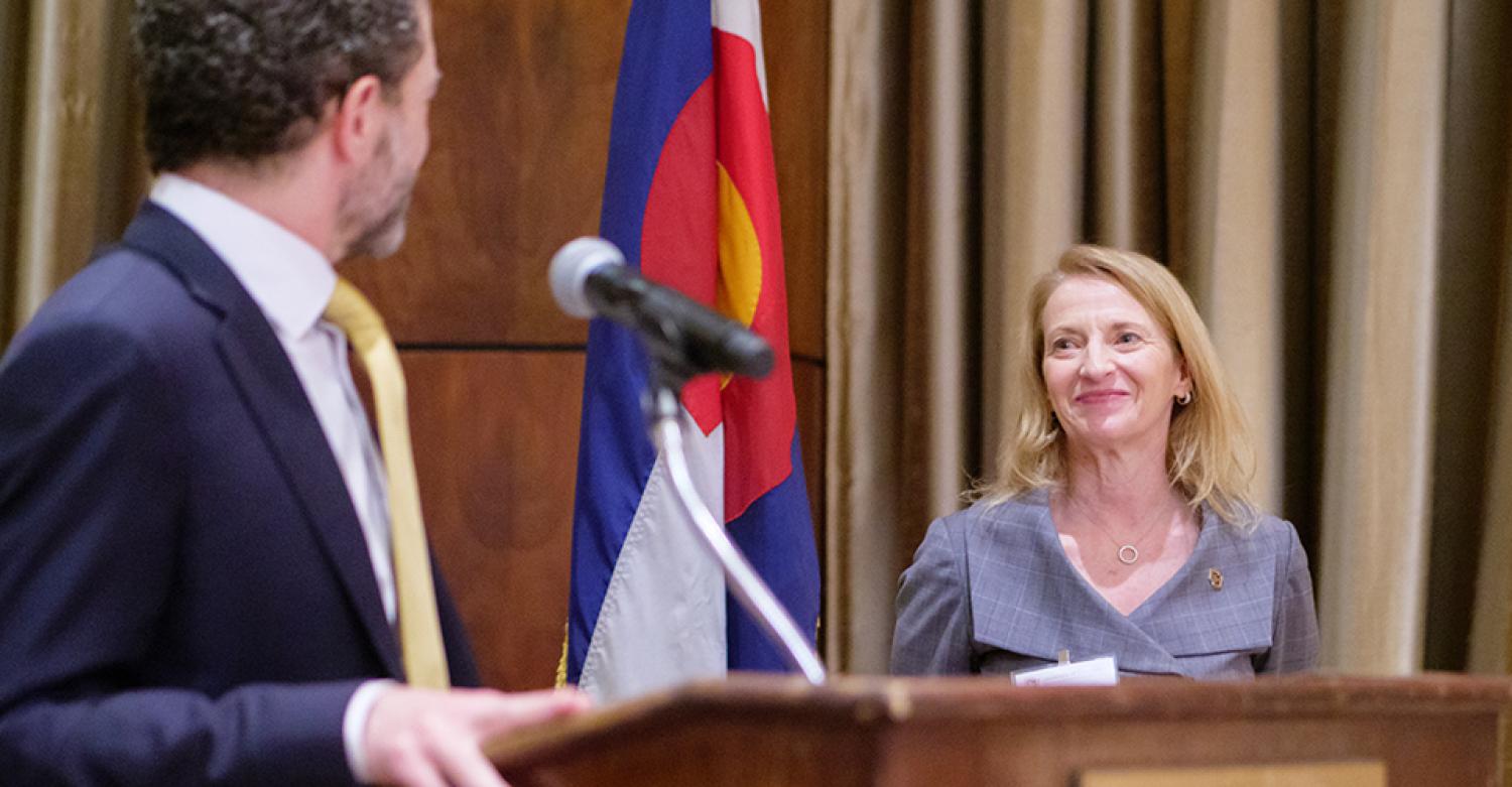 The dean stands facing the camera. The president's back is to the camera as he greets her.
