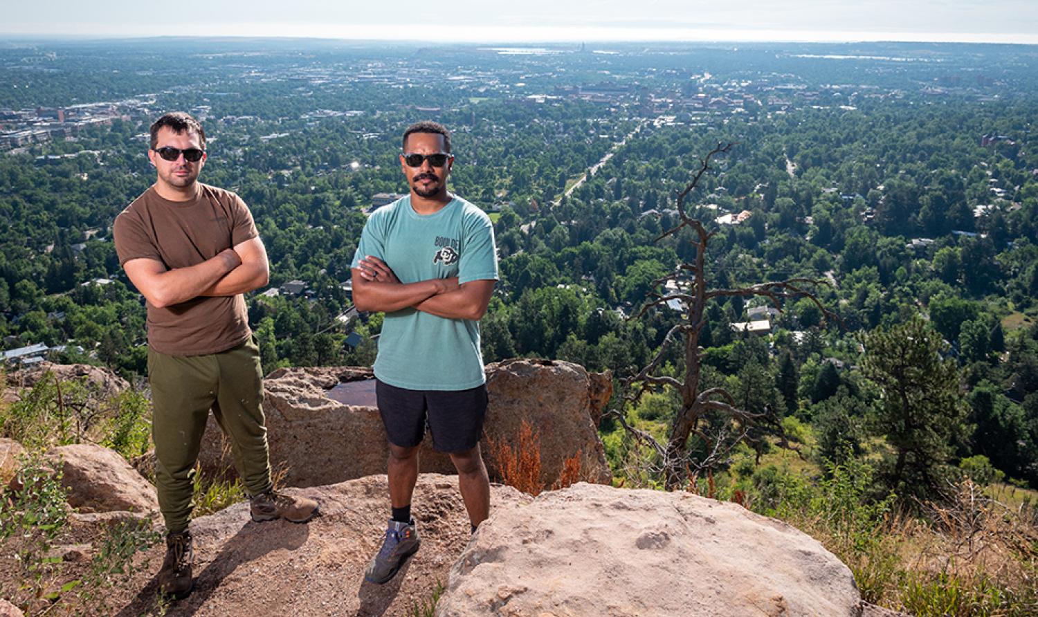 Two alumni and veterans stand on a cliff overlooking Boulder.
