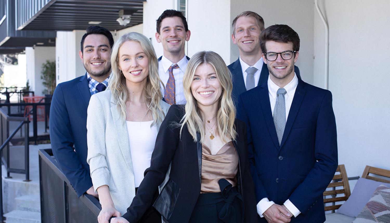 Four male and two female students pose as a group in professional dress.