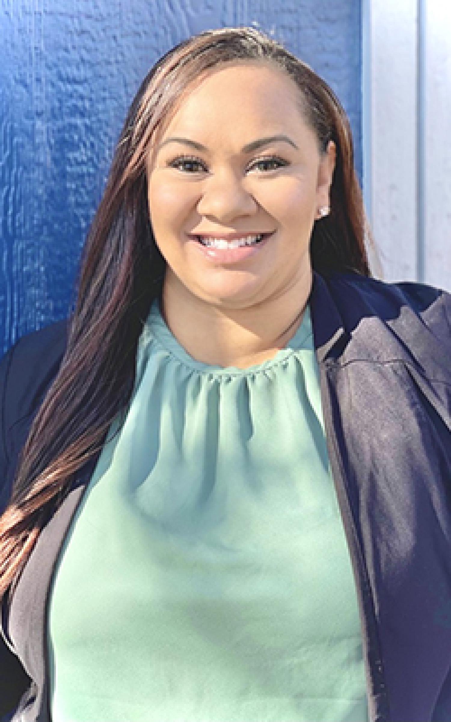 Shay Cardenas in professional attire, against a blue backdrop.