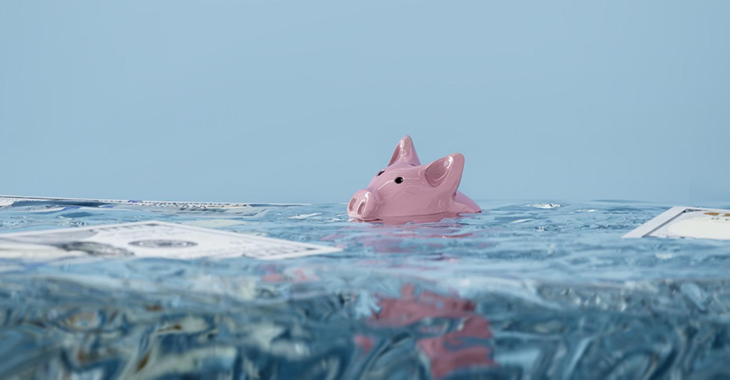 A piggy bank is mostly underwater in a pool. Also floating is U.S. paper currency.