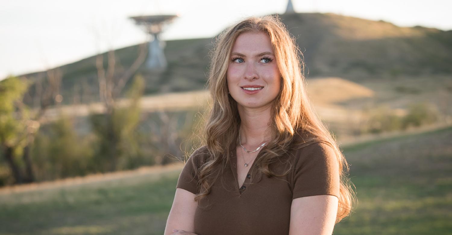 Taylor Bata stands in a field with satellite dishes in the background.