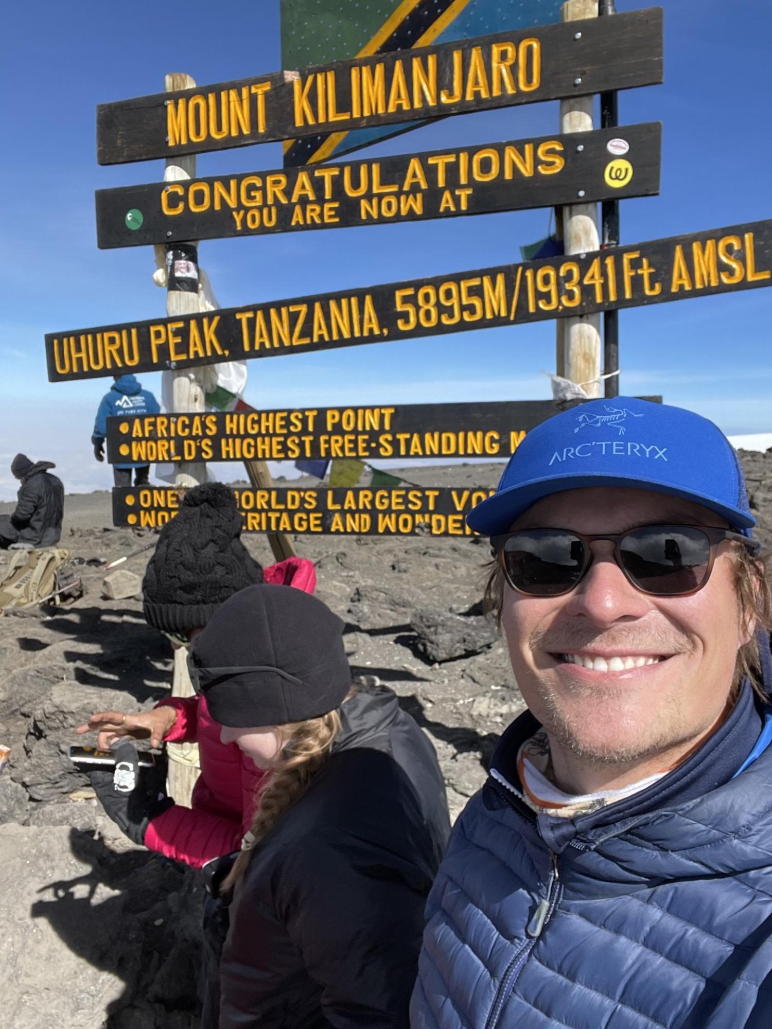 Henry Coote smiling in from of the top of Mount Kilimanjaro