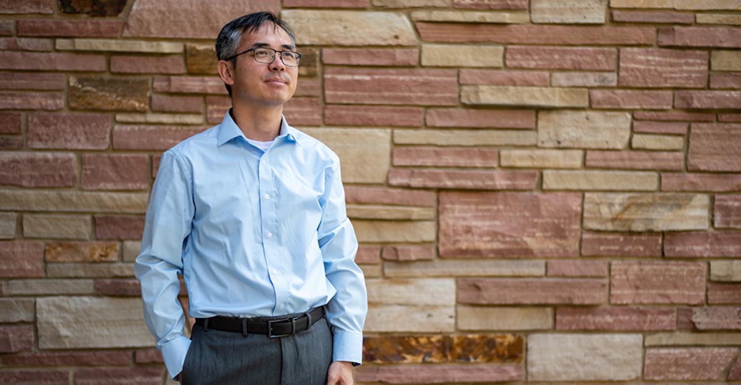 Dan Zhang in a relaxed pose near a brick wall.