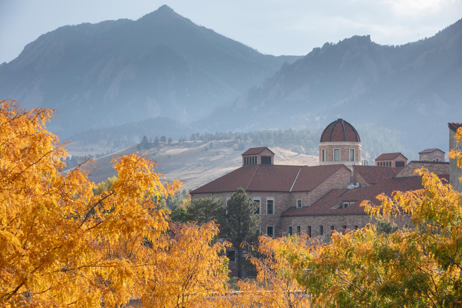 Koelbel Building shot from afar on an overcast day. Gold leaves are visible in the foreground while the Flatirons are visible in the background.