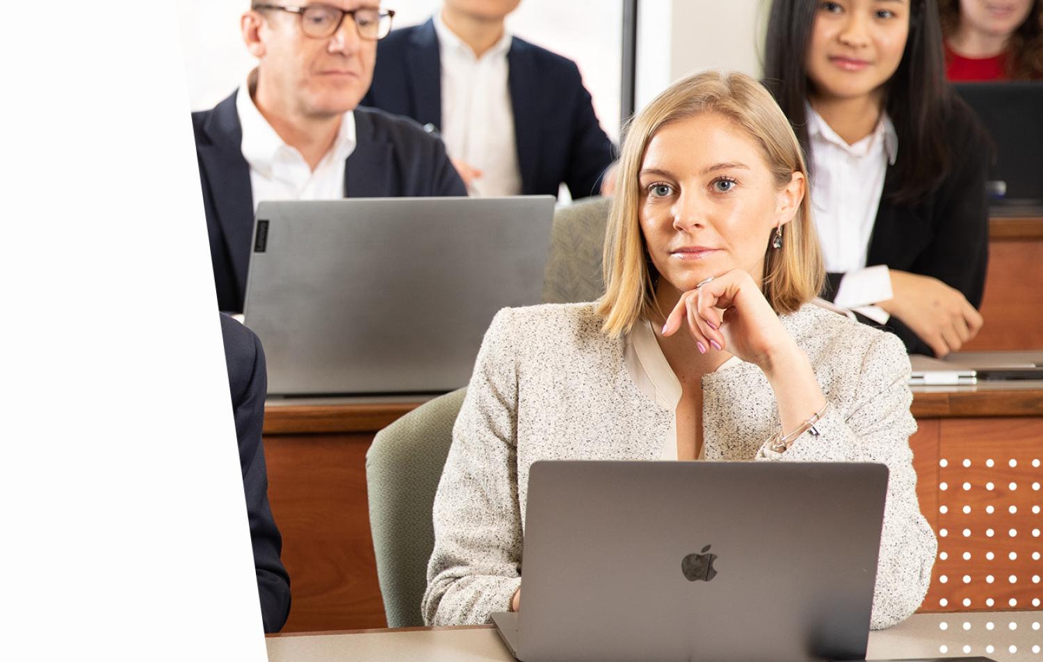 Woman listens with interest in a classroom as she sits with a laptop in front of her.