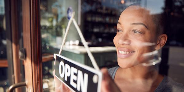 A woman flips the Open sign over on her restaurant as she looks out the window.