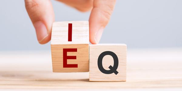 A hand turns a wooden blocks from "E" to "I", while a stationary block shows the letter "Q"