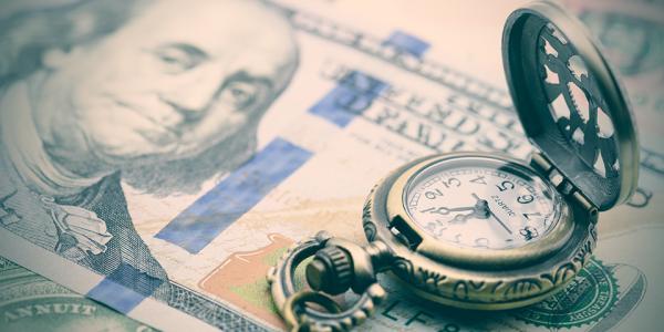 A vintage pocket watch opened upon a stack of hundred-dollar bills.