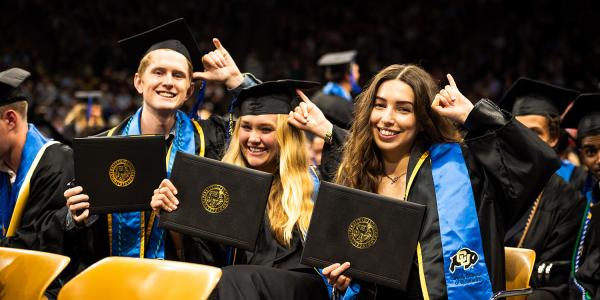 Graduates smile for the camera while holding up their diplomas.