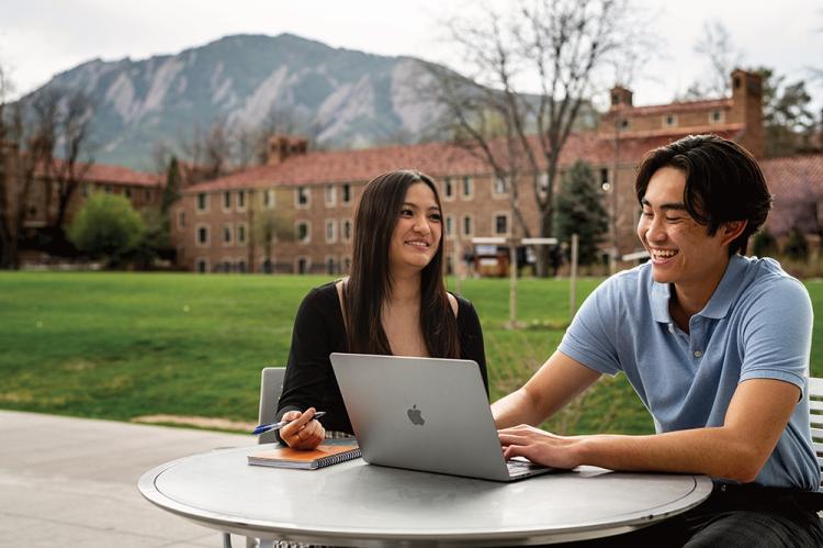 Julie Hoang and Kevin Nguyen share a laugh while meeting at an outdoor table of CU Boulder's campus.