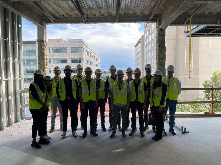 Members of the Graduate Real Estate Association pose wearing hard hats and neon vests at a construction site