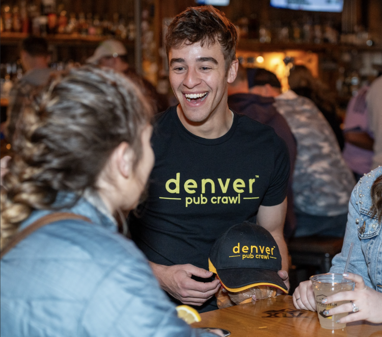 Man smiles while in conversation wearing a Denver Pub Crawl T-shirt