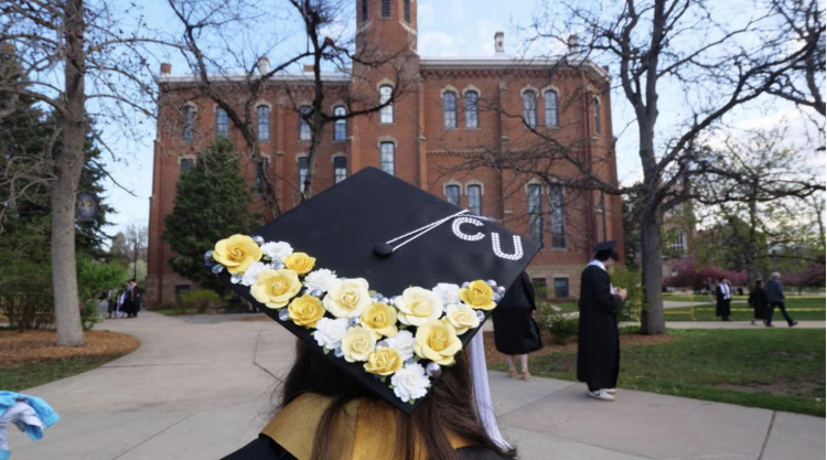 A student with a decorated graduation cap looks out at campus