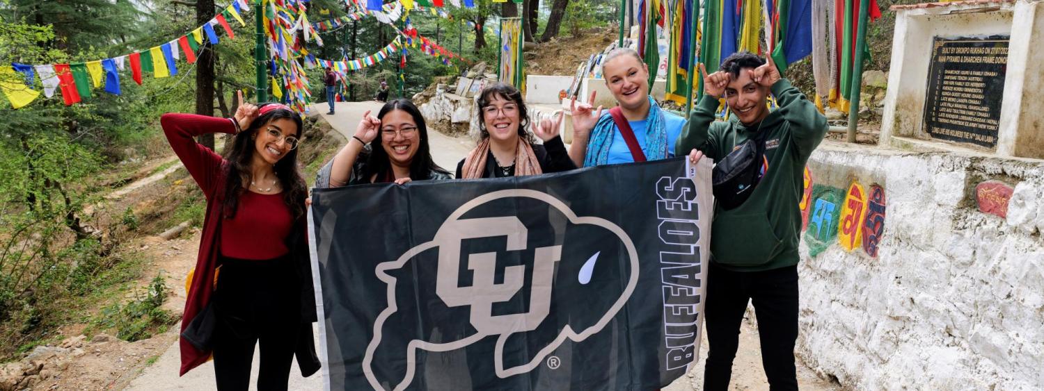 Students pose with a CU flag while holding up Buff horns