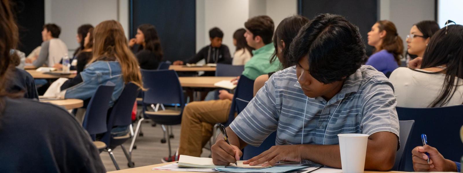 A male student is taking notes during a Business at a Glance academic session.