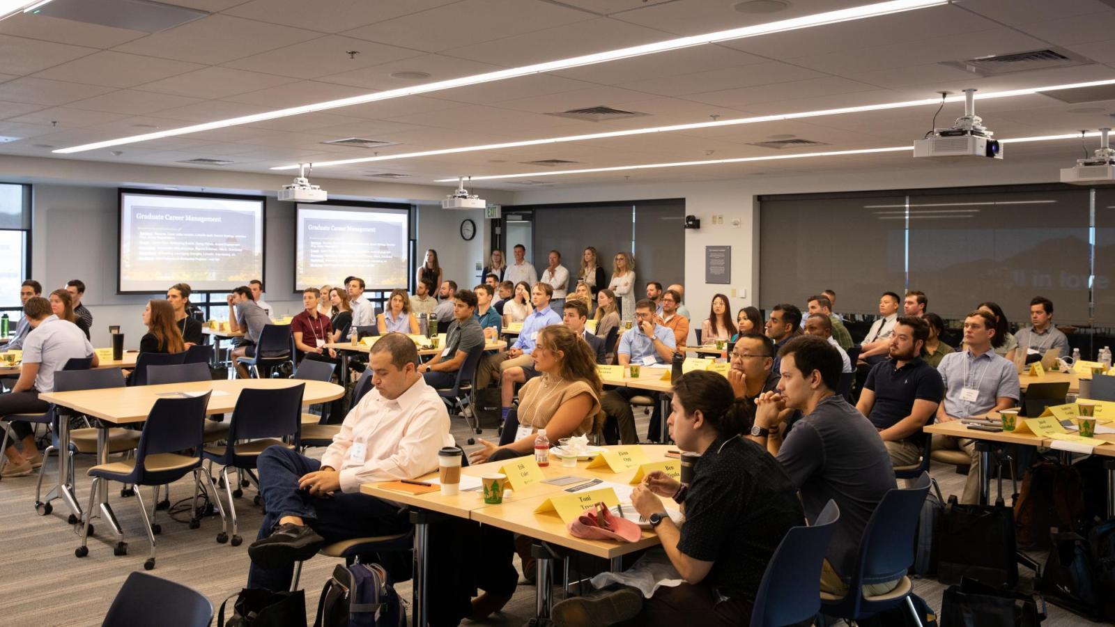 MBA students sit in a classroom and listen to a speaker as they attend orientation