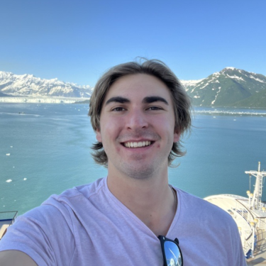 Sean Boselli posing in front of a lake with mountains behind it.