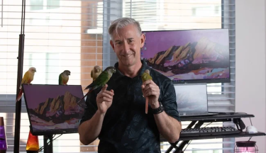 Russell Jeans poses with his parrots in front of a home work station