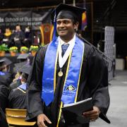 Atul, in graduation regalia, walks down the aisle at commencement.