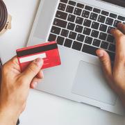 A woman pays her credit card balance using a laptop. The card is visible in the foreground.