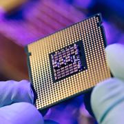 A worker holds a semiconductor chip up for inspection before adding it to a computer processor.