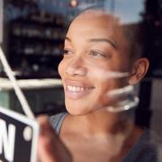 A woman flips the Open sign over on her restaurant as she looks out the window.