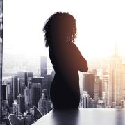 A young woman, silhouetted in a conference room, looks out onto the city skyline.