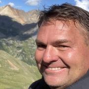 John Quinn on a hiking trail. Mountains are visible in the back.