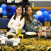 Mackenzie Culver and Rhiannon Martin posing with their backs together at a table.