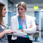 Three female professionals in business attire chat in a corridor in the Koelbel Building.