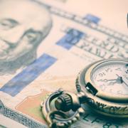 A vintage pocket watch opened upon a stack of hundred-dollar bills.