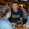 Man smiles while in conversation wearing a Denver Pub Crawl T-shirt 