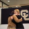 Two people hug with a CU logo in the background