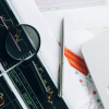 Overhead photo of desk with a laptop, financial chart, pen, magnifying glass