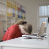 Woman leans forward, touching her head to her desk in frustration