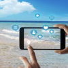 Person takes a smart phone photo of a beach; social media reactions pop out of the screen