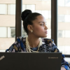 A woman working on a laptop gazes off to the side