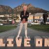 Elex Ayala standing in from of the mountains in Cape Town, South Africa, on top of a "Live on" sign