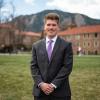 Andy Stasch smiles while posing on the CU Boulder campus with the Flatirons in the distance.