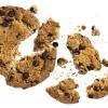 A chocolate chip cookie broken into many pieces against a white backdrop.