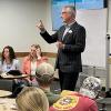 Clark Jones, in a suit, makes a point in the front of a crowded classroom. Other students look back to see the student Clark is talking to.