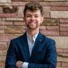 Matei in business casual attire, standing against a sandstone brick wall.