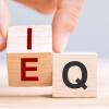 A hand turns a wooden blocks from "E" to "I", while a stationary block shows the letter "Q"
