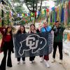 Students pose with a CU flag while holding up Buff horns