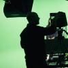 Silhouette of people against a green screen. Recording equipment is visible in the foreground.