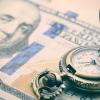 A vintage pocket watch opened upon a stack of hundred-dollar bills.
